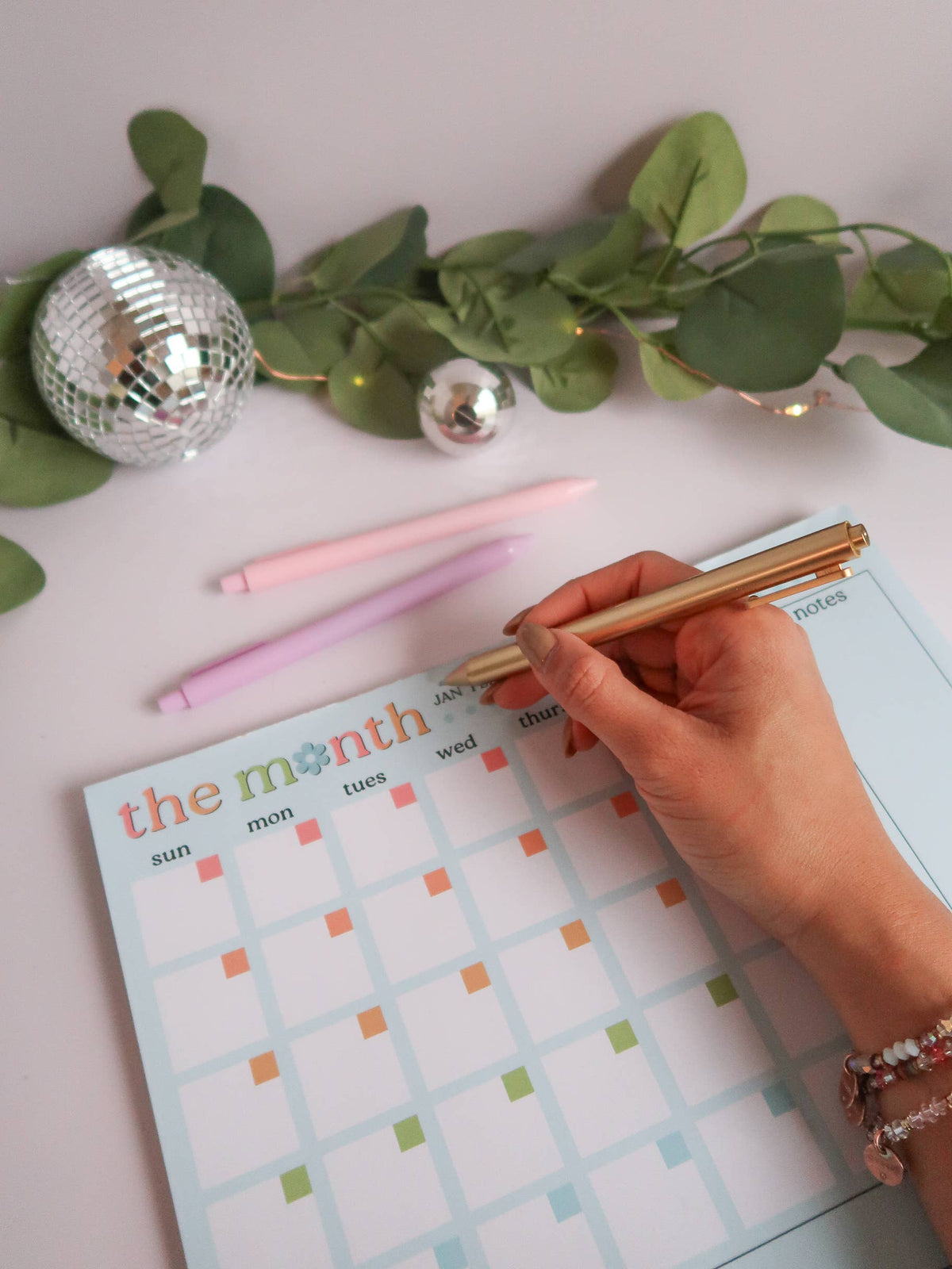 Hand writing on a planner with decorative elements on a light pink surface