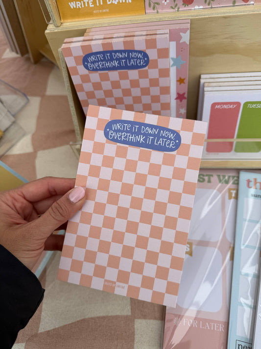 Checkered notepad with text held by a hand, with more notepads in the background.