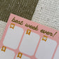 A close-up of a pink weekly planner sticker sheet with the text 'best week ever!' and labeled boxes for Monday through Sunday, placed on a woven green and white checkered fabric background.
