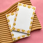 Two notepads with smiley face border design on a pink background