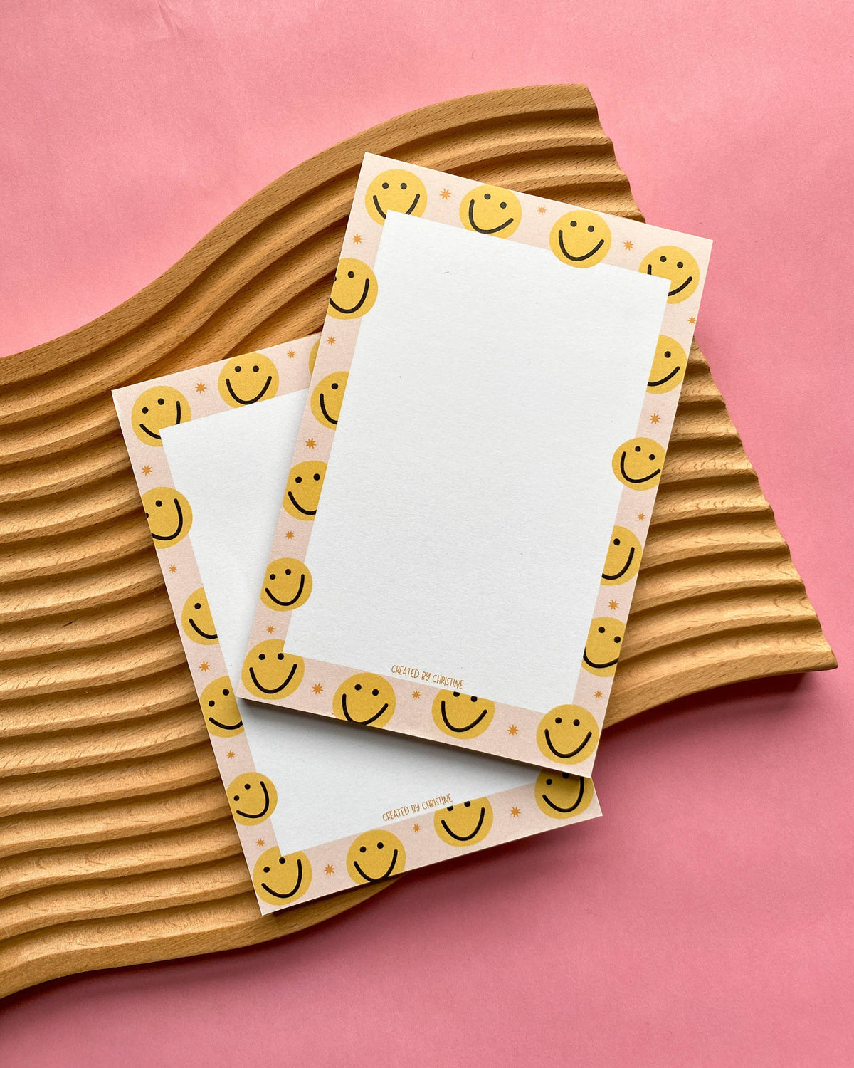 Two notepads with smiley face border design on a pink background