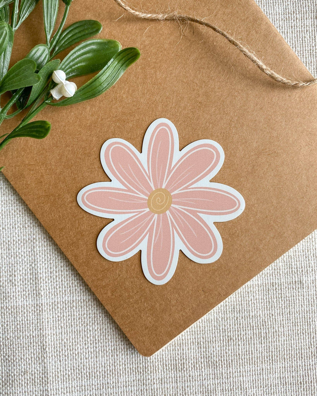 A die-cut Magnet shaped like a daisy flower with pink petals, a white border, and a beige center, placed on a brown kraft paper envelope with green leaves in the corner.