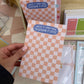Checkered notepad with text held by a hand, with more notepads in the background.